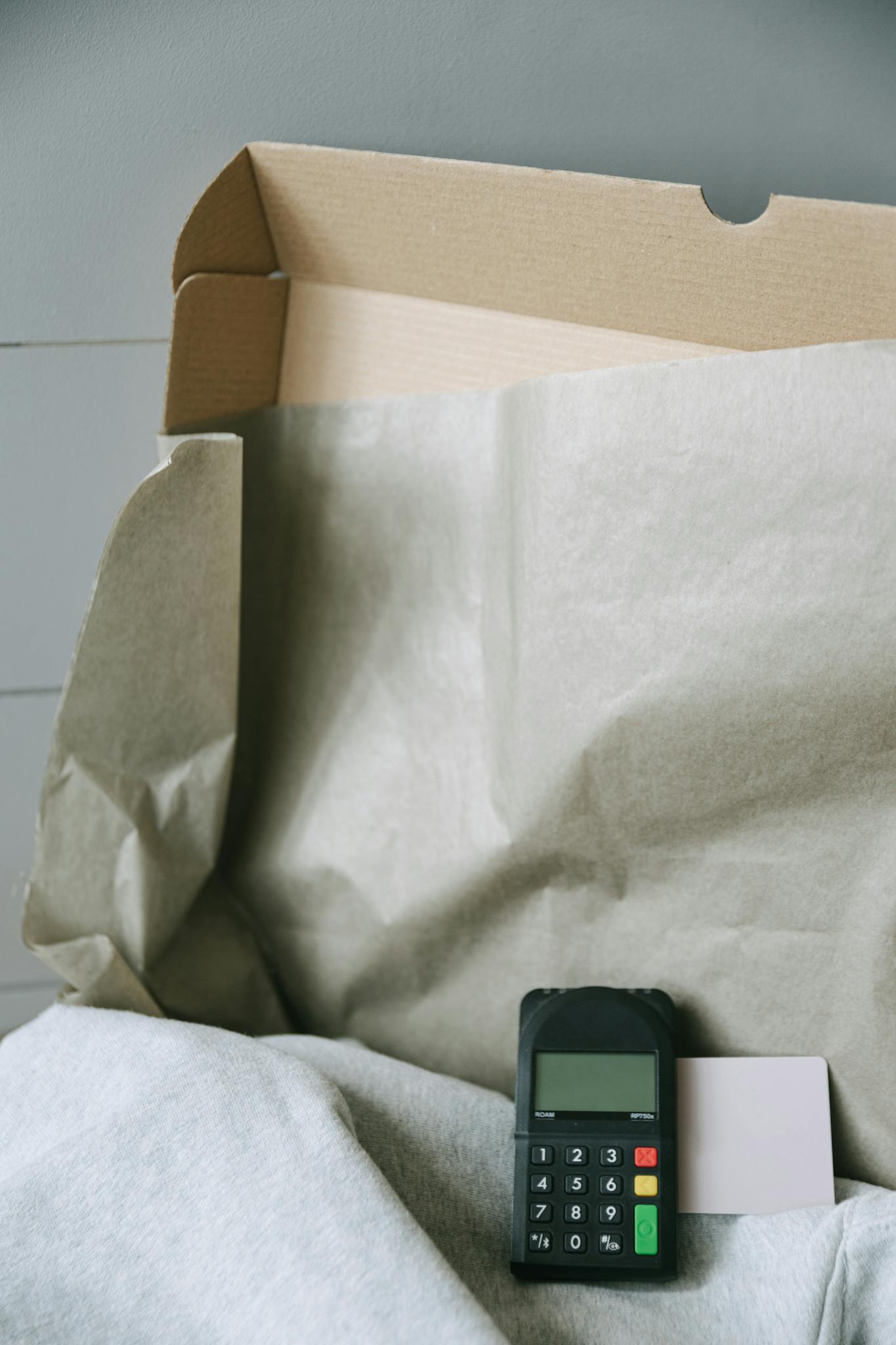 Image of a payment terminal with a cardboard box and paper, representing online shopping and contactless payment.